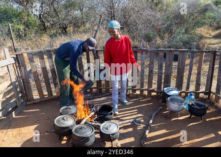 Kochen im Kessel dreibeinige Pot afrikanische Küche im Freien, Straßenverkäufer afrikaner, Paare Mann und Frau kochen für Leute auf der Straße Stockfoto