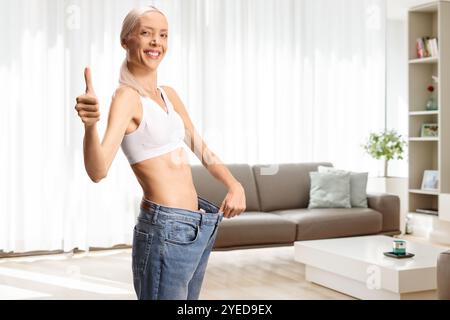 Eine glückliche schlanke Frau, die eine Jeans anzieht und die Daumen nach oben drückt Stockfoto