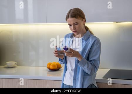 Ungesunde runzelnde Frau hält Pillen Flasche, Glas Wasser lesen Medikamente Anweisungen zu Hause. Stockfoto