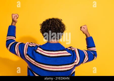 Foto-Porträt des attraktiven jungen Mannes Rückansicht Gewinn erhöhen Fäuste gekleidet stilvolle blau gestreifte Kleidung isoliert auf gelbem Farbhintergrund Stockfoto