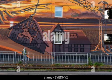 27.10.2024 Breslau, Polen. Der Mann geht neben ein buntes Wandgemälde, das einen Kran vor dem Hintergrund des Sonnenuntergangs darstellt. Urbane Kunst, Straßenkultur und Architektur Stockfoto