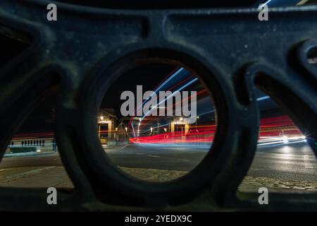 Lichtspuren von Autos, die nachts die Brücke überqueren, durch ein Loch in einer Metallkonstruktion gesehen Stockfoto