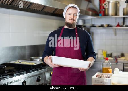 Bärtiger Arbeiter, der mit leerem Tablett in der Küche des Deli-Kaufhauses steht Stockfoto