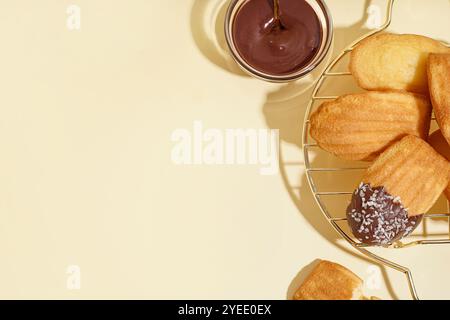 Raster mit köstlichen Madeleinen und Schüssel Schokoladenpaste auf beigem Hintergrund Stockfoto