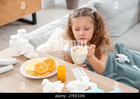 Ein krankes kleines Mädchen mit Halsschmerzen, das eine Tasse Zitronentee aus dem Regal zu Hause nimmt Stockfoto