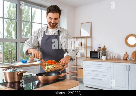 Hübscher bärtiger Mann, der geschnittenes Gemüse in die Pfanne in der Küche steckt Stockfoto