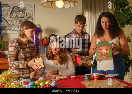 Eine Familie versammelt sich an einem Tisch, der für die Feiertage dekoriert ist. Vier Personen verpacken Geschenke mit buntem Geschenkpapier und Dekorationen Stockfoto