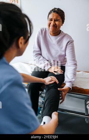 Ängstliche junge Frau, die ihr Bein von einer ärztlichen Fachärztin im Untersuchungsraum untersuchen lässt Stockfoto