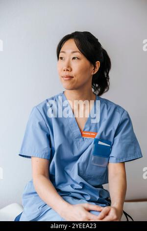 Nachdenkliche Ärztin, die vor der Wand sitzt Stockfoto