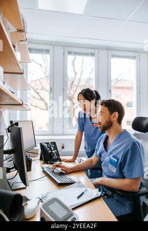 Fokussierte männliche und weibliche medizinische Fachkräfte, die am Computer im Untersuchungsraum arbeiten Stockfoto