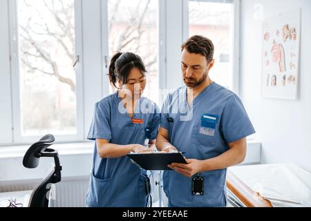 Weibliche medizinische Expertin diskutiert mit männlichem Kollegen, der im Krankenhaus eine Klemmplatte hält Stockfoto