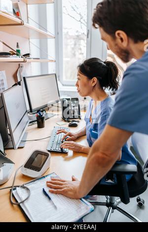 Fokussierte Ärztin, die am Computer arbeitet, während sie mit einer Kollegin in in der Klinik arbeitet Stockfoto
