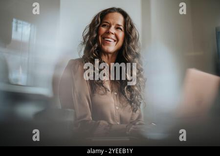 Glückliche, reife Geschäftsfrau mit langen braunen Haaren, die im Büro arbeitet Stockfoto