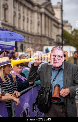 London, Schiedam, Großbritannien. 30. Oktober 2024. Ein Demonstrant, der den britischen Premierminister Keir Starmer verkörpert, benutzt eine Vuvuzela als Hörgerät - was bedeutet, dass er taub gegenüber den Aufrufen der WASPI ist. Am 30. Oktober 2024 protestierten Mitglieder der britischen Interessenvertretungsgruppe WASPI (Women Against State Pension Injustice) vor den Houses of Parliament. Sie forderten eine Entschädigung für Frauen, die von den Änderungen der Rentengesetze in den Jahren 1995 und 2011 betroffen waren. (Kreditbild: © James Petermeier/ZUMA Press Wire) NUR REDAKTIONELLE VERWENDUNG! Nicht für kommerzielle ZWECKE! Stockfoto