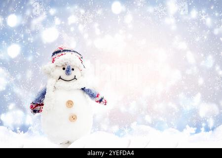 Ein fröhlicher Schneemann in einem farbenfrohen Winterhut und Schal, der vor einem schneebedeckten, glitzernden Hintergrund mit Bokeh-Lichtern steht Stockfoto