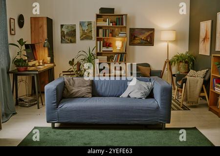 Dunkelblaues Sofa mit zwei Baumwollkissen in der Mitte des Wohnzimmers mit komfortabler Arbeitszone voller Zimmerpflanzen und Stockfoto