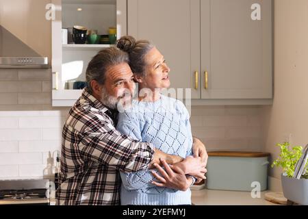 Glückliches, reifes Paar, das sich in einer gemütlichen Küche umschließt, einen friedlichen Moment zusammen, zu Hause Stockfoto