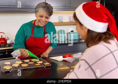 Ältere Freundinnen schmücken zusammen Weihnachtskekse, lachen in der Küche, zu Hause Stockfoto