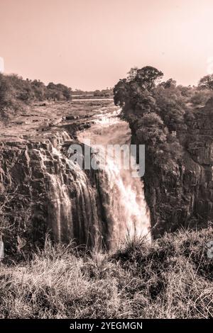 Ein großer Wasserfall, der inbrünstig über felsige Klippen sprudelt und von Bäumen umgeben ist und die Kraft und Schönheit der Natur in rauem Gelände darstellt. Stockfoto