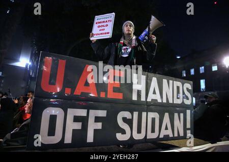 Ein Demonstrant mit einem Megaphon und einem Schild steht hinter einem Banner, auf dem während der Demonstration ëUAE Hands Off Sudan' steht. Demonstranten versammeln sich gegenüber der Downing Street, um gegen die Mittäterschaft der Emirate am Völkermord im Sudan zu demonstrieren. Sie fordern das Ende des Leidens und dass die VAE, die die Rapid Support Forces (RSF) finanzieren und unterstützen, das Land verlassen. Die Organisation Action for Sudan steht für Menschenrechte, Gerechtigkeit und Selbstbestimmung des sudanesischen Volkes. Demonstranten versammelten sich gegenüber der Downing Street, um sich gegen die angebliche Unterstützung der Rapid Support for durch die VAE zu wehren Stockfoto