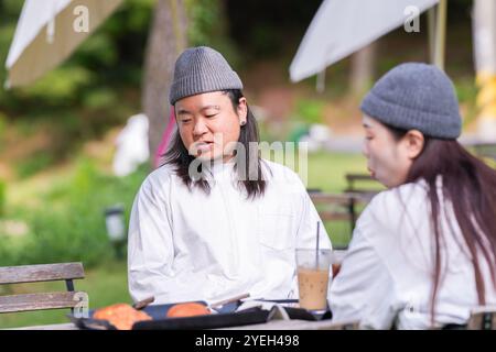 Ein koreanischer Mann und eine Japanerin, beide im Alter von 30 Jahren und ein verheiratetes Paar, genießen in einem stilvollen Café im Herbst einen Brunch mit drei Hunden Stockfoto