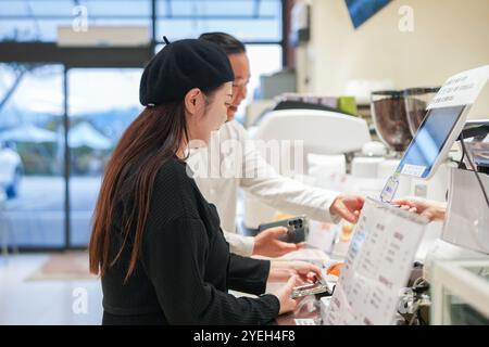 Ein koreanischer Mann im Alter von 30 Jahren und eine Japanerin, die ein verheiratetes Paar ist, bestellen an der Theke eines stilvollen Cafés in Gosan-RO, Nam Stockfoto