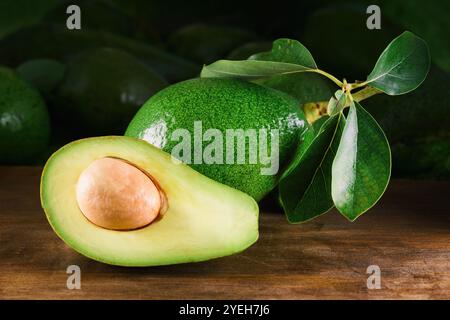 Frische, reife grüne Avocado mit Blättern auf Holztisch Stockfoto