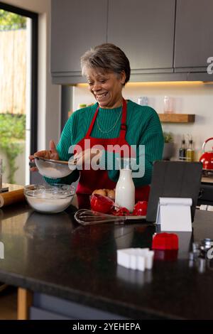 Weihnachten, lächelnde Seniorin in der Küche, Mehl gesiebt, Weihnachtsgeschenke zuhause zubereitet Stockfoto