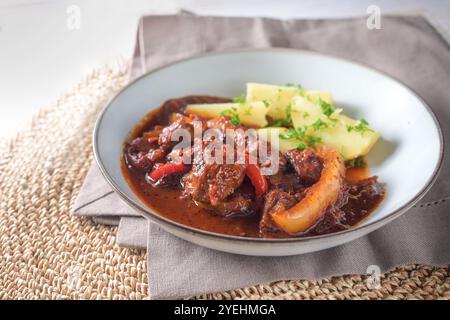 Gulasch mit Paprika in ungarischer Art serviert mit Kartoffeln und Petersilie auf einem hellgrauen Teller, scharfes Fleischgericht zum Abendessen oder Mittagessen, Kopie Stockfoto