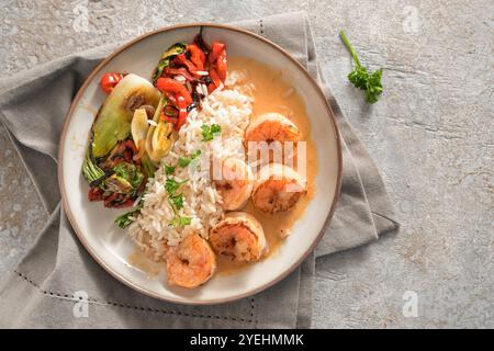 Gebratene Garnelen mit Krustentiersauce, Reis und Gemüse auf einem beigefarbenen Teller und Serviette auf einem Steingrund, in asiatischem Stil kochen, Blick von oben Stockfoto