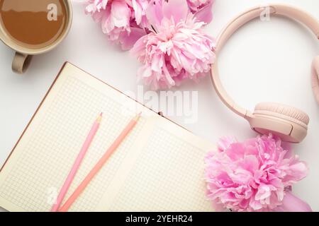 Moderne pinkfarbene Kopfhörer mit Blumen-Pfingstrosen und Notizbuch auf hellem Hintergrund. Draufsicht Stockfoto