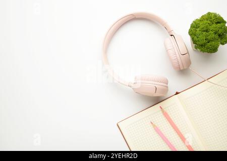 Moderne pinkfarbene Kopfhörer mit Pflanzen und Notebook auf hellem Hintergrund. Draufsicht Stockfoto