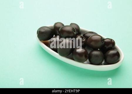 Frische Oliven auf weißer Platte auf minzfarbigem Hintergrund. Draufsicht Stockfoto