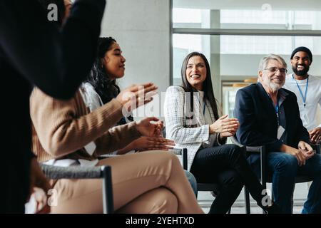 Vielfältige Gruppe von Fachleuten, die aktiv an einer Unternehmenskonferenz teilnehmen. Die Teilnehmer sind engagiert, klatschen und lächeln. Stockfoto