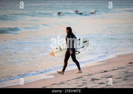 Ein Surfer, der am Strand entlang läuft und ein Surfbrett trägt. Stockfoto
