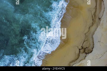 Drohnenaufnahme, Strand, Meer, Wellen, Blick aus der Vogelperspektive auf Meereswellen, die auf einen Sandstrand stürzen, wodurch dynamische Texturen und eine ruhige Atmosphäre entstehen Stockfoto