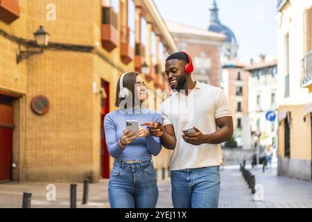 Multiethnische Paare, die das Mobiltelefon benutzen und Musik hören, wenn sie die Straße hinunter laufen Stockfoto