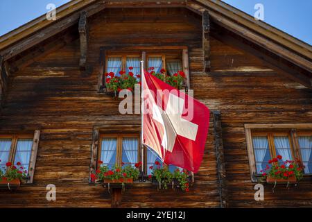 Wunderschöne Altstadt mit einem Holzhaus mit Blume und Schweizer Flagge an einem sonnigen Sommertag in Andermatt, URI, Schweiz, Europa Stockfoto