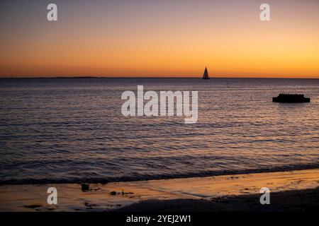 Das Bild fängt einen ruhigen Sonnenuntergang über dem Meer ein, mit warmen Orange- und Violetttönen, die sich auf dem Wasser spiegeln. Stockfoto