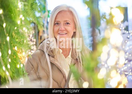 Eine Frau lächelt vor einem Weihnachtsbaum. Sie trägt eine braune Jacke und ein weißes Hemd Stockfoto