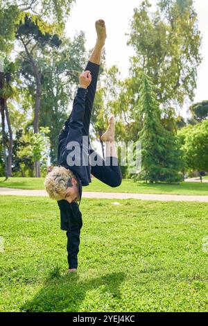 Junger Mann springt und tanzt zeitgenössisches Ballett im Park mit urbaner Tracht. Stockfoto