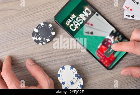 Online-Casino-Spiele mit Handeingabe eines mobilen Geräts und Gegenständen auf Holztischen spielen. Draufsicht. Stockfoto