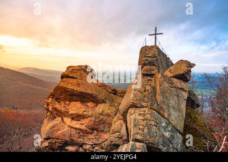 Die Sonne untergeht hinter der Granitformation Oresnik und beleuchtet ein hölzernes Gipfelkreuz am Aussichtspunkt in Hejnice, Isergebirge, und bietet einen atemberaubenden Blick auf die Landschaft. Stockfoto