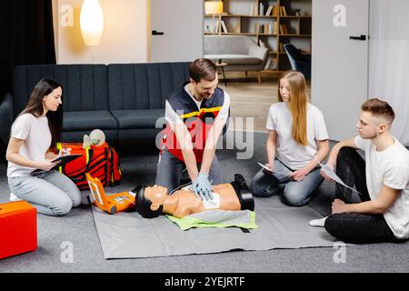 Junger Ausbilder, der bei der Durchführung von Herzkompressionen mit dem Dummy während des Gruppentrainings im Innenbereich hilft. Stockfoto