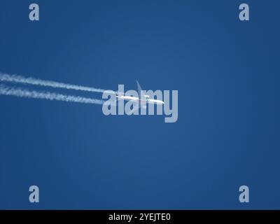 Ein Emirates-Jet-Flugzeug, das in großer Höhe in blauem Himmel mit Kondensstreifen fliegt Stockfoto