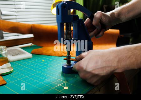 Nahaufnahme der Hände des Meisters, die handgefertigte Lederprodukte nähen. Ein Männerbräuner verbindet die Teile und schafft hochwertige Lederaccessoires. Arbeitsvorgang Stockfoto