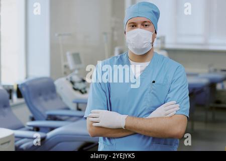 Porträt des Chirurgen, der in der Klinik mit gekreuzten Armen steht und Selbstvertrauen und Professionalität zeigt, ausgestattet mit medizinischen Maschinen im Hintergrund Stockfoto