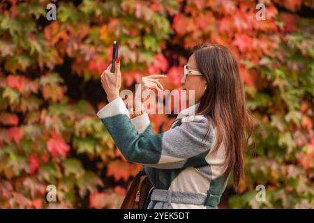 London, Großbritannien. 31. Oktober 2024 Awoman fotografiert mit einem Mobiltelefon vor der farbenfrohen Ausstellung von Virginia Creeper, die die Wand der Admiralität Citadel in Horse Guards Parade Credit bedeckt. Amer Ghazzal/Alamy Live News Stockfoto