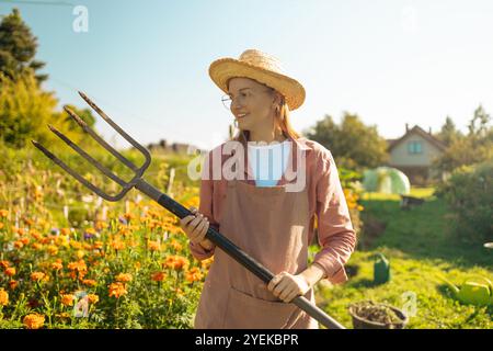 Schöne kaukasische Farmerin, die früh am Morgen mit Heugabel auf dem Feld spaziert. Lebensstil in der Landwirtschaft. Weibliche Gabel und Arbeit im Freien Stockfoto