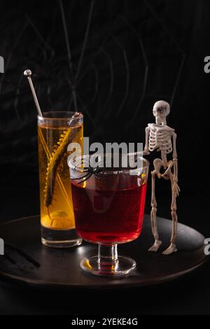 Halloween-Cocktails in Rot und Orange und Mocktails dekoriert Spinne und Skelett auf schwarzem Hintergrund. Horror-lustiges Getränk für festliche Party. Stockfoto